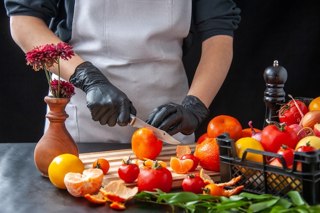 Front view female cook cutting tangerines on a dark cooking salad health diet vegetable meal food fruit job