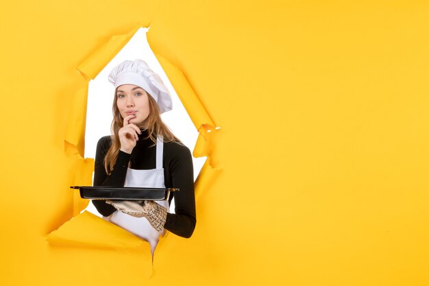 Вид спереди женщина-повар держит черную сковороду с печеньем на желтом эмоции солнце еда фото работа кухня кухня цвет
