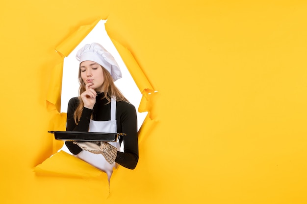 Front view female cook holding black pan with biscuits on yellow emotion sun food photo job kitchen cuisine color