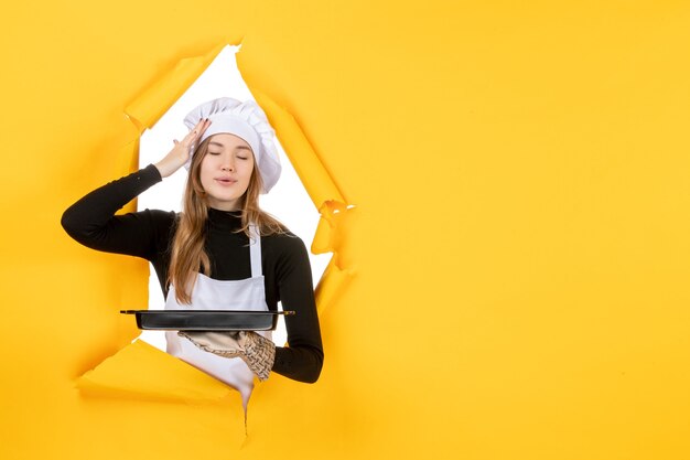 Вид спереди женщина-повар держит черную сковороду на желтой эмоции, солнце, еда, работа, кухня, кухня, цвет