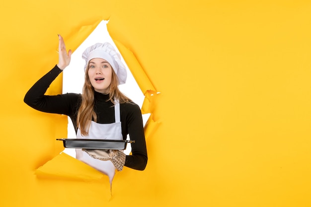 Cuoca vista frontale che tiene padella nera su emozioni gialle cibo solare lavoro fotografico cucina cucina colore