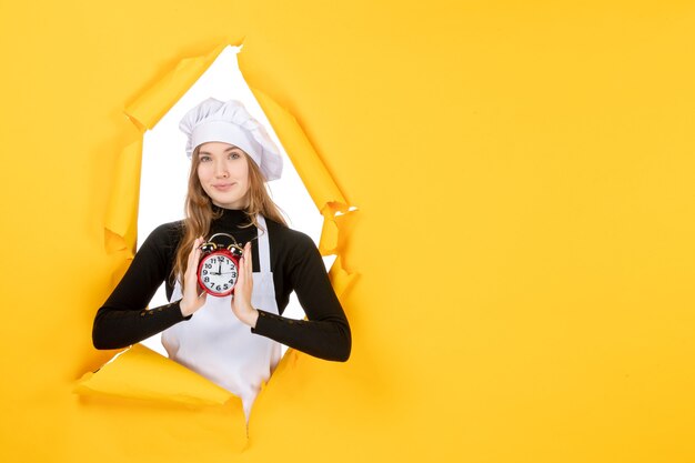 Front view female cook holding clock on the yellow photo color job cuisine kitchen sun food emotion time