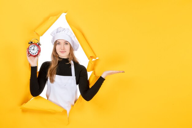 Front view female cook holding clocks on yellow food photo color job emotion time sun