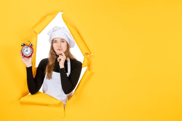 Front view female cook holding clocks on yellow food photo job kitchen emotion sun cuisine color