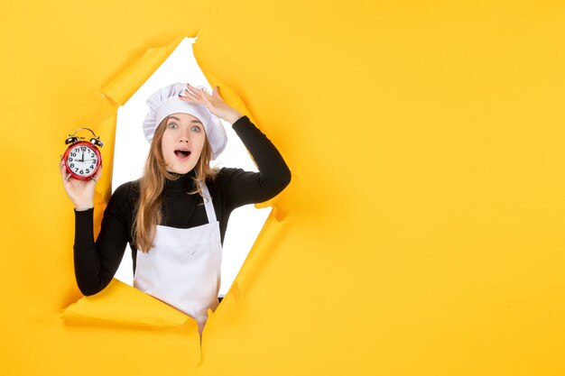 Front view female cook holding clocks on yellow time food photo job kitchen emotion sun cuisine colors