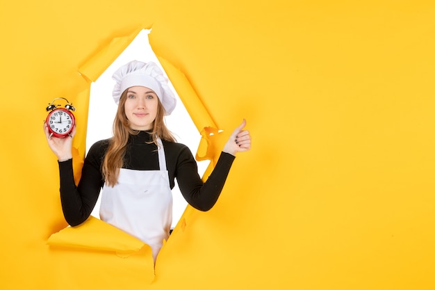 Front view female cook holding clocks on yellow time food photo job kitchen sun cuisine color