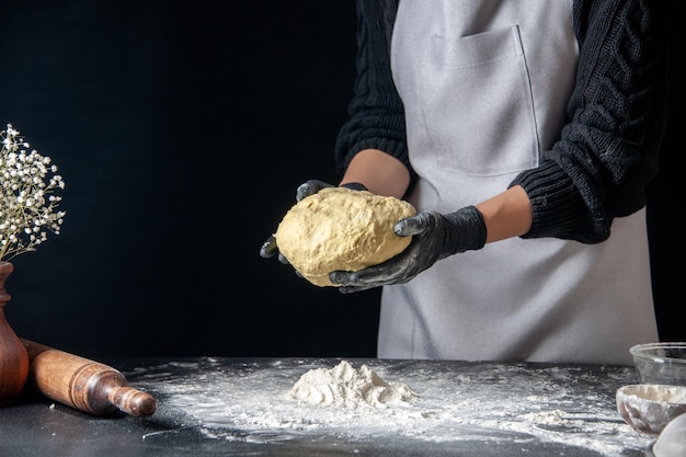 Вид спереди женщина-повар держит тесто на темном тесте, яичная работа, пекарня, горячее тесто, кухня, кухня