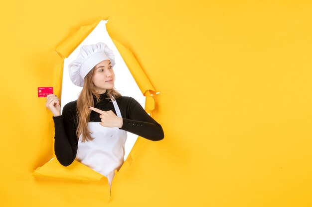 Вид спереди женщина-повар держит красную банковскую карту на желтых деньгах, цветная работа, фото, кухня, кухня, эмоция, еда.