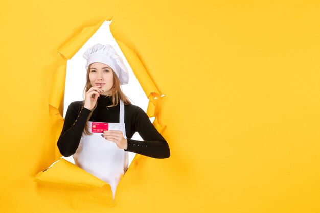 Front view female cook holding red bank card on yellow photo emotion kitchen cuisine color money job