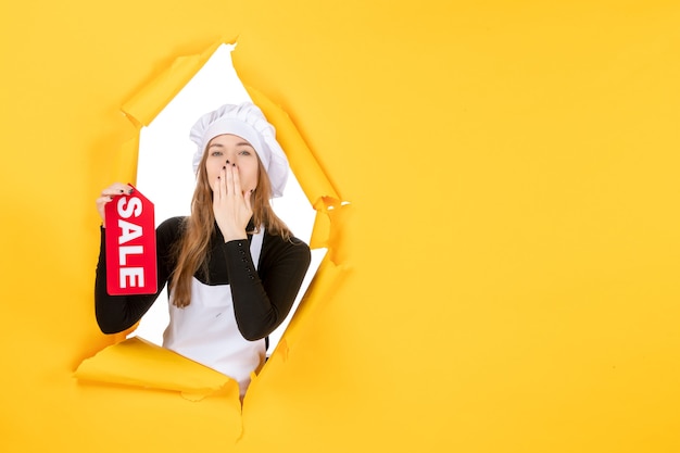 Foto gratuita cuoca di vista frontale che tiene la vendita rossa che scrive sul lavoro di colore giallo cucina cucina emozione cibo