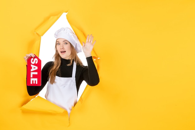 Foto gratuita cuoca di vista frontale che tiene la vendita rossa che scrive sulla foto di emozione della cucina della cucina di lavoro di colore giallo