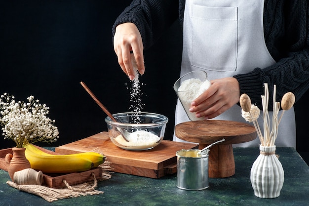 Cuoca di vista frontale che versa la noce di cocco nel piatto con latte condensato su fondo scuro