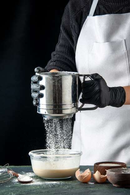 Front view female cook pouring flour into eggs on dark hotcake pastry cake pie cuisine dough worker