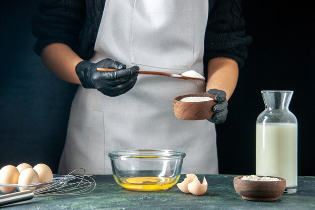 正面図女性料理人が暗いペストリーケーキパイベーカリー労働者のホットケーキ料理の仕事で生地のために卵に小麦粉を注ぐ