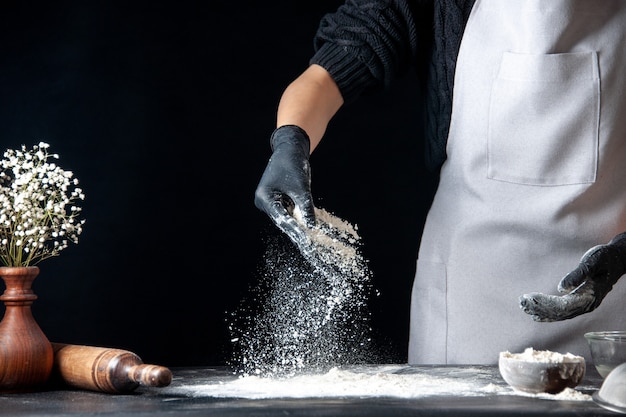 Front view female cook pouring flour on table for dough on a dark dough egg job bakery hotcake pastry kitchen cuisine