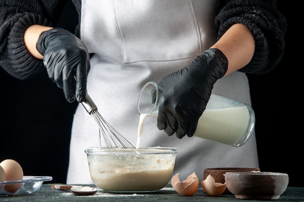 Free photo front view female cook pouring milk into eggs and sugar for dough on dark hotcake pastry cake pie cuisine job worker