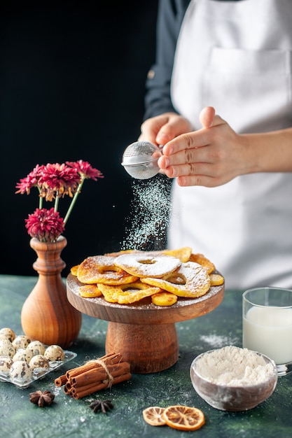 Front view female cook pouring sugar powder on dried pineapple rings on dark fruit cooking job cake pie bakery