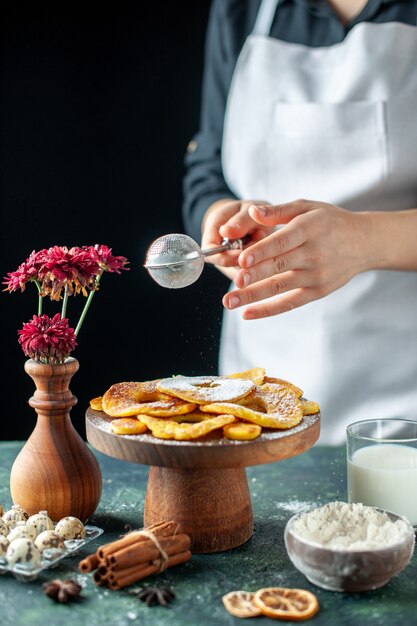 Front view female cook pouring sugar powder on dried pineapple rings on a dark fruit cooking job pastry cake pie bakery