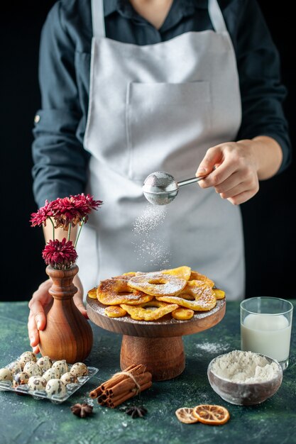 Front view female cook pouring sugar powder on dried pineapple rings on a dark fruit cooking job worker pastry cake pie bakery