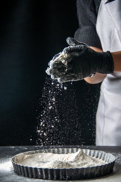 Front view female cook pouring white flour into the pan on dark egg cake bakery cuisine pie hotcake kitchen dough