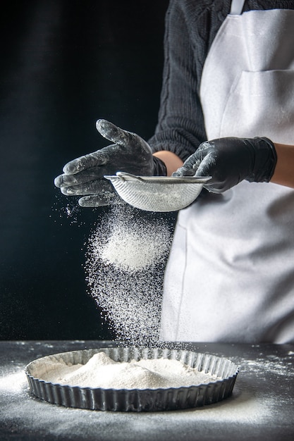 Front view female cook pouring white flour into the pan on dark egg cake bakery pastry cuisine dough pie hotcake