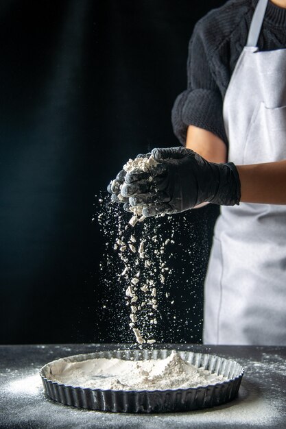 Front view female cook pouring white flour into the pan on dark egg cake bakery pastry cuisine pie hotcake kitchen dough