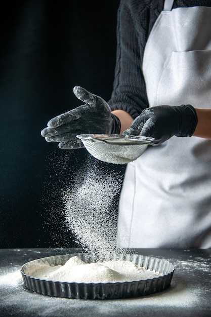 Front view female cook pouring white flour into the pan on dark egg cake bakery pastry kitchen cuisine dough hotcake