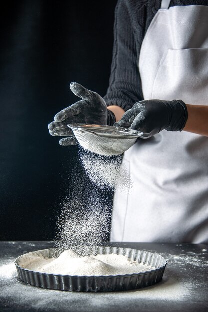 正面図女性料理人が暗い卵ケーキベーカリーペストリーキッチン料理パイホットケーキの鍋に白い小麦粉を注ぐ