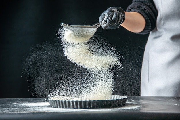 Front view female cook pouring white flour into the pan on dark egg job bakery pastry kitchen cuisine dough