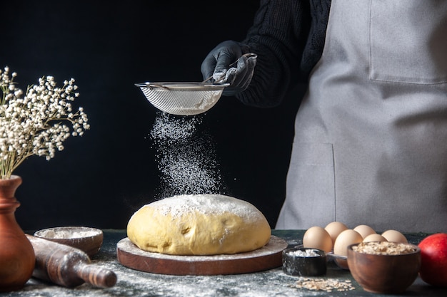 正面図女性料理人が暗いペストリーの仕事で生の生地に白い小麦粉を注ぐ生の生地ホットケーキベーカリーパイオーブン