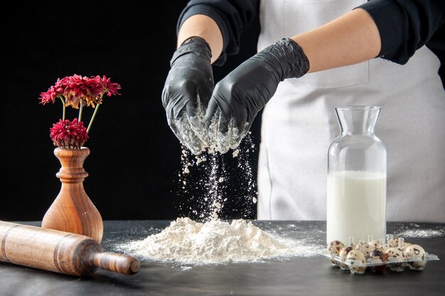 正面図女性料理人が暗い仕事で生地のためにテーブルに白い小麦粉を注ぐペストリーパイベーカリー料理生地焼きケーキビスケット