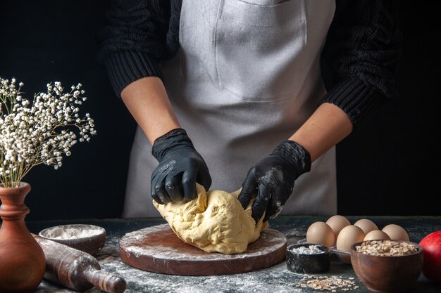 Front view female cook rolling out dough on a dark job raw dough hotcake bakery pie oven pastry