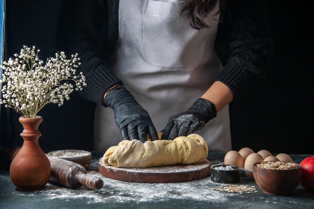 Foto gratuita cuoco femminile di vista frontale che stende la pasta sul forno della torta del forno del hotcake crudo del lavoro della pasticceria scura