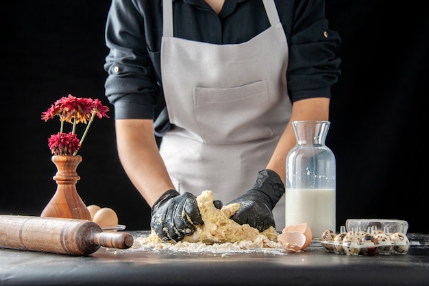 Бесплатное фото Вид спереди женщина-повар раскатывает тесто на темной работе, выпечка пирога, выпечки бисквитного теста