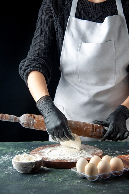 Front view female cook rolling out dough with flour on dark cake job oven hotcake pie worker egg cuisine dough