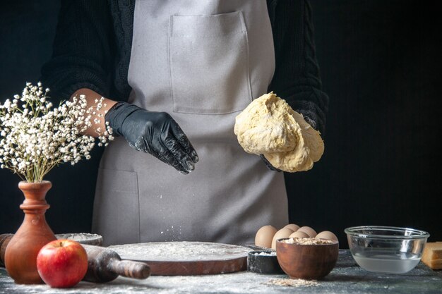 正面図女性料理人が暗い生地のペストリーキッチンのホットケーキ料理ベーカリーの卵に小麦粉で生地を広げています