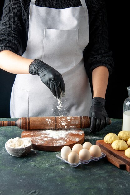 Front view female cook rolling out dough with flour on dark job cuisine hotcake raw bake cake pie worker