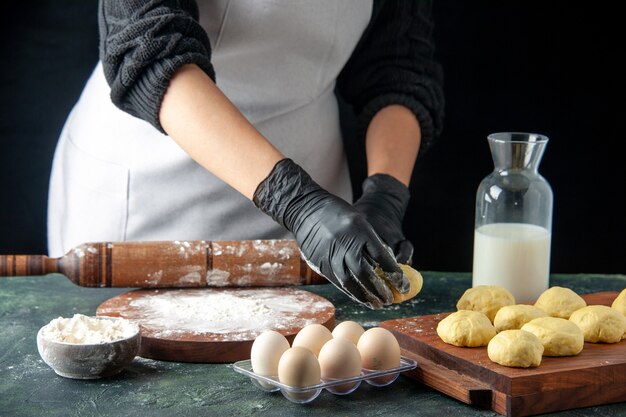 Front view female cook rolling out dough with flour on dark job cuisine oven hotcake dough bake cake pie worker egg