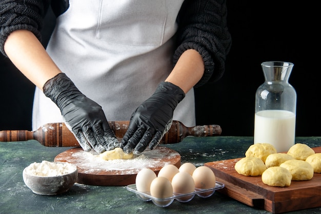 Front view female cook rolling out dough with flour on a dark job cuisine oven hotcake