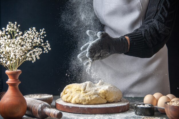 Front view female cook rolling out dough with flour on a dark job raw dough bakery pie oven pastry hotcake