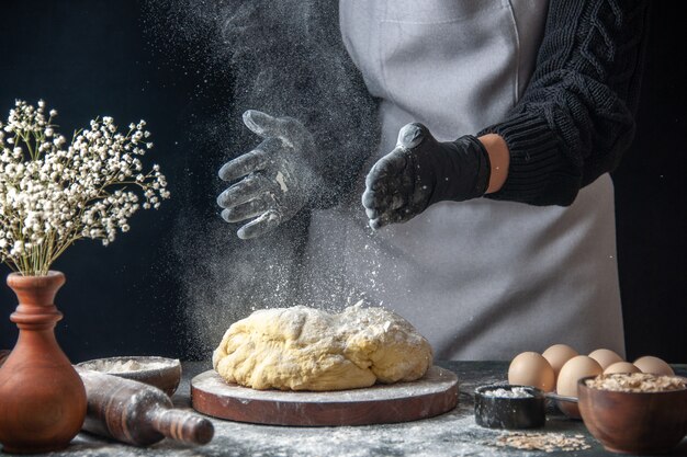 Front view female cook rolling out dough with flour on dark job raw dough bakery pie oven pastry hotcake