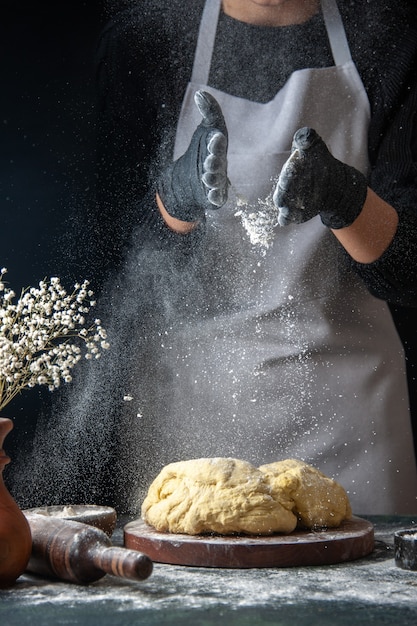 Front view female cook rolling out dough with flour on a dark job raw dough hotcake bakery pie oven pastry