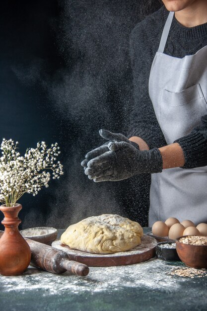 正面図女性料理人が暗い仕事で小麦粉で生地を広げている生の生地パイオーブンペストリーホットケーキベーカリー