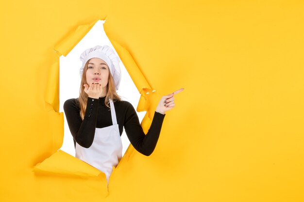 Вид спереди женщина-повар, отправляющая воздушные поцелуи на желтой кухне, фото, еда, кухня, работа, цветная бумага, солнце