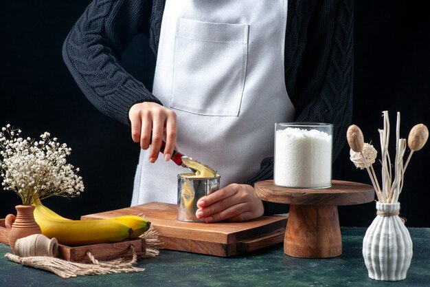 Front view female cook trying to open can with condensed milk on dark background