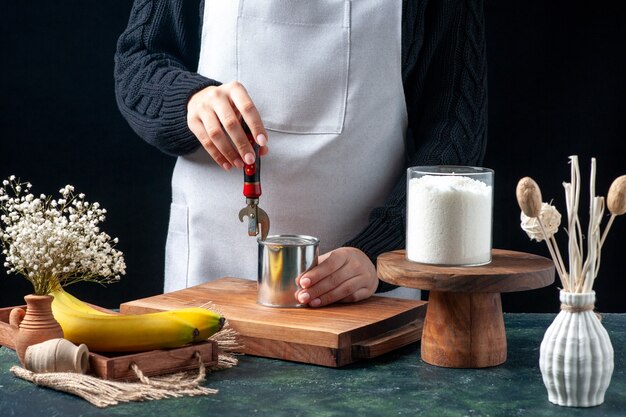 Front view female cook trying to open can with condensed milk on dark background