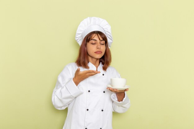 Cuoco femminile di vista frontale in vestito bianco del cuoco che tiene tazza di tè su una scrivania verde