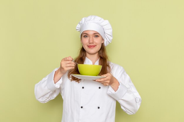 Front view of female cook in white cook suit holding green plate on green wall