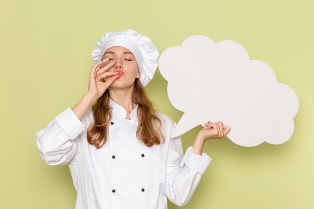 Front view of female cook in white cook suit holding a huge white sign on the green wall