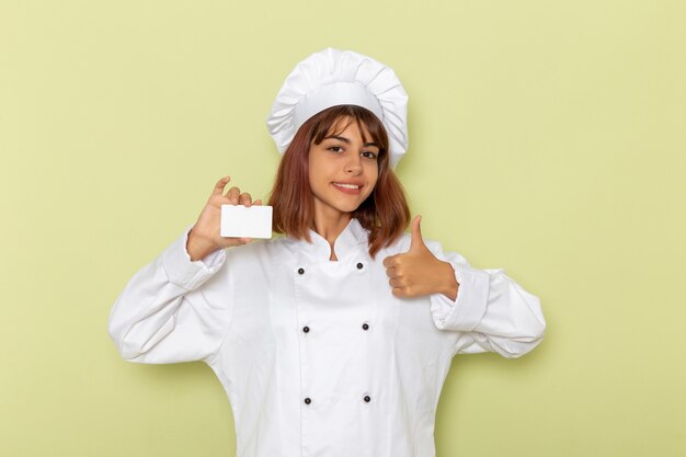 밝은 녹색 표면에 흰색 카드를 들고 흰색 요리사 정장에 전면보기 여성 요리사